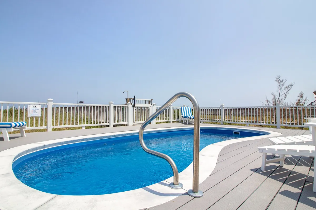 A sparkling saltwater swimming pool surrounded by poolside seating and a privacy fence, with a clear blue sky overhead. The inviting outdoor setting is perfect for family swim sessions, sunbathing, and poolside relaxation.