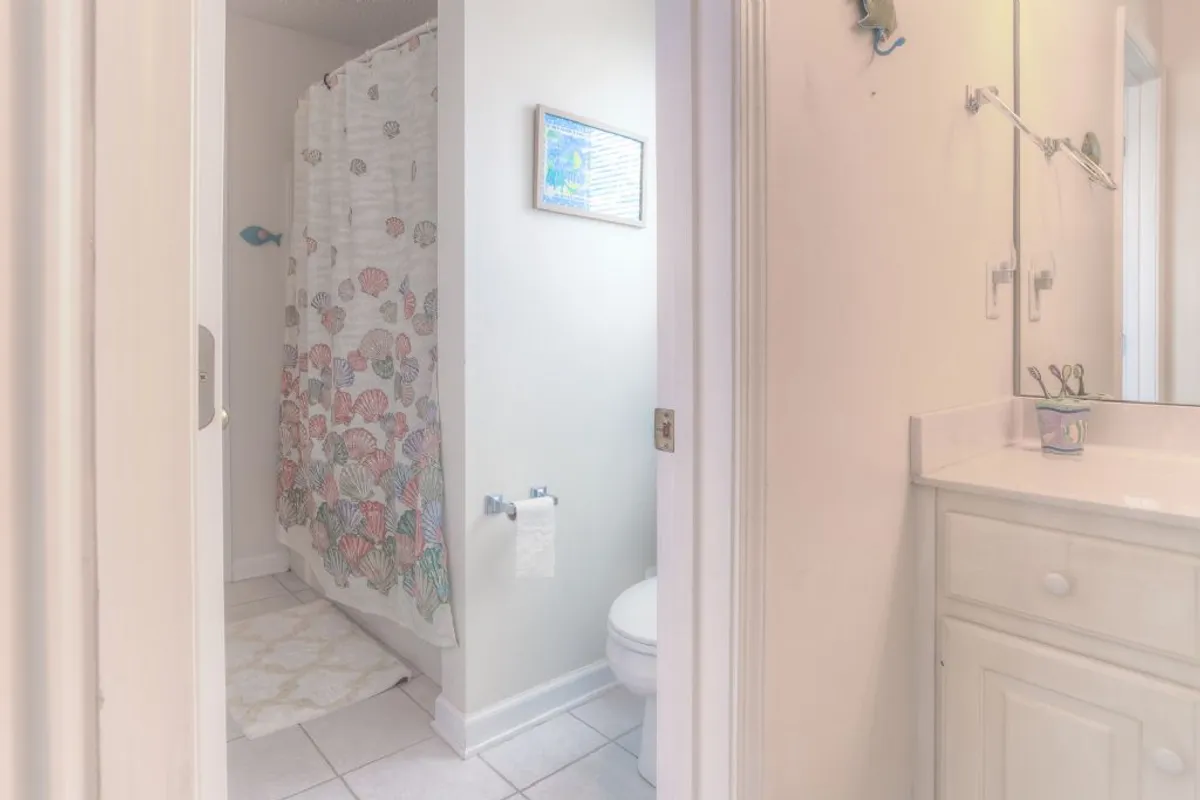 A bright and refreshing bathroom with a colorful shower curtain, a sleek bathroom vanity, and decorative wall art. The space is designed for quick and easy routines, perfect for freshening up after a day at the beach or for guest convenience.