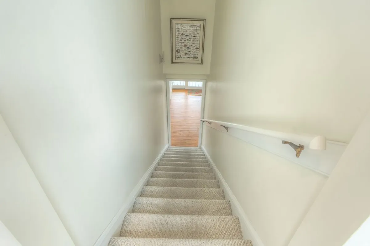 An interior hallway with a clean staircase, doorway, and framed artwork, suggesting access to various parts of the home. The area is uncluttered, making it easy for large groups to move in and settle quickly.