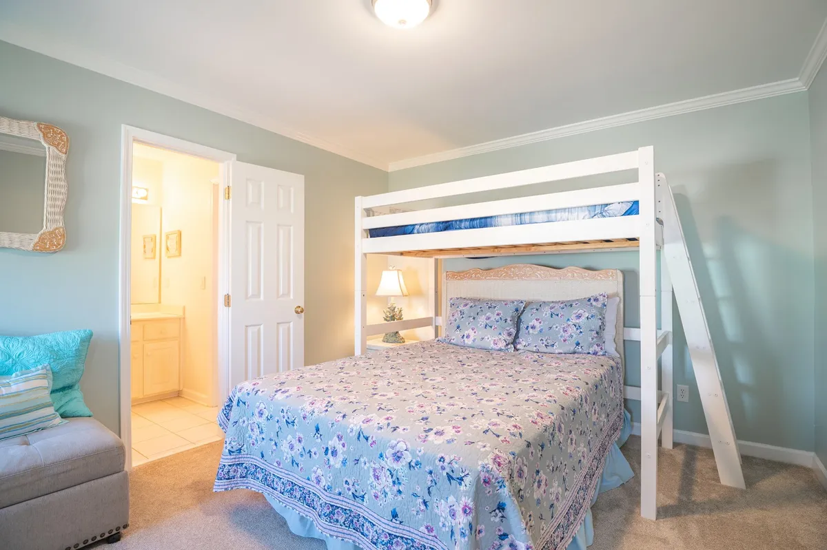 A cozy bunk room with a bunk bed featuring floral bedding, a mirror, and a soft sofa. The inviting space is ideal for children or friends, perfect for sleepovers or sharing stories.