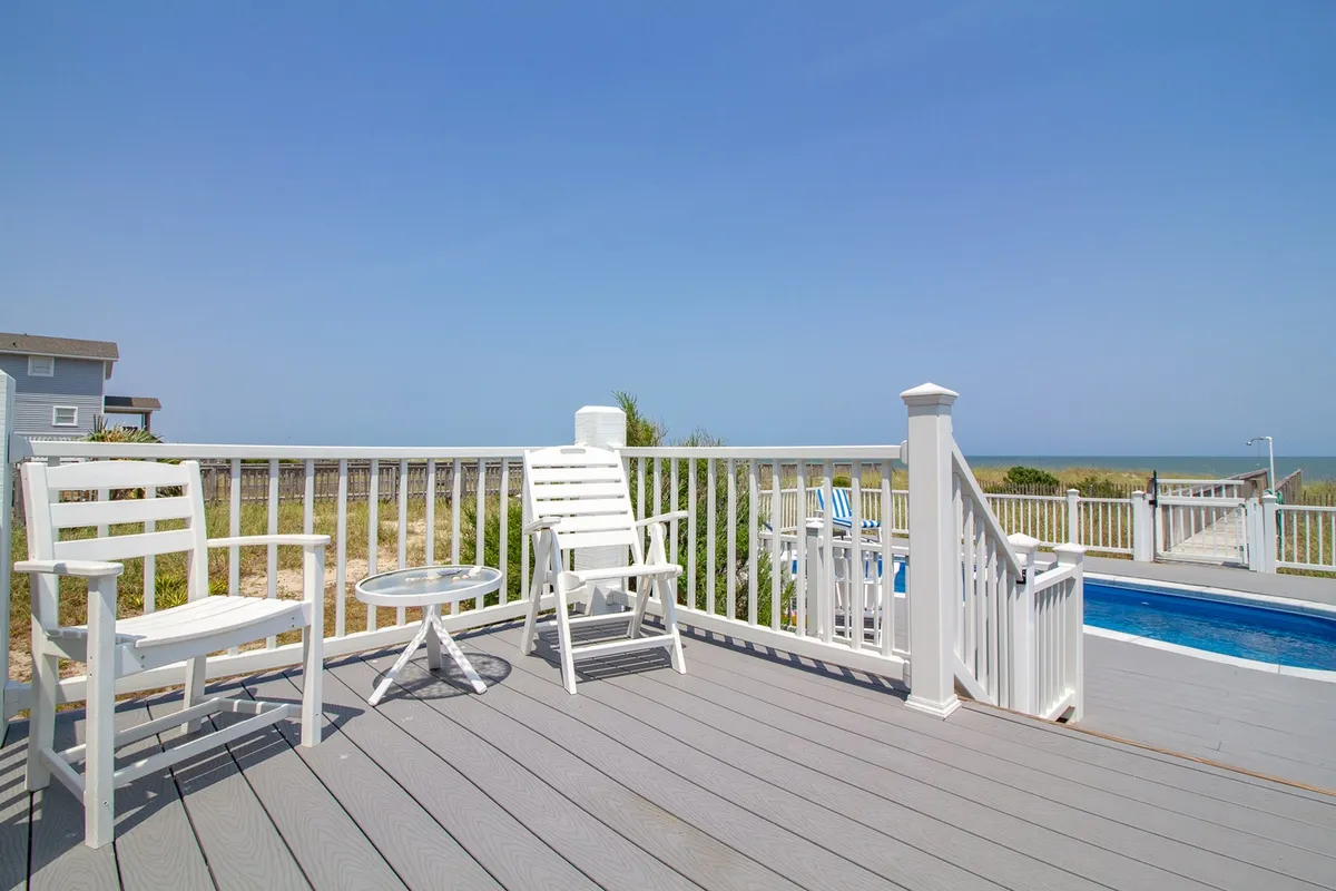 This serene poolside view includes white chairs and a small table overlooking the pool and ocean. The area is set up for relaxation, reading, or sharing a drink—all with stunning ocean views as a backdrop.